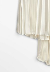 Couches de tissu plissé couleur crème avec une texture transparente et fluide suspendues sur un fond blanc.