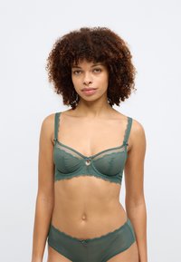 Πράσινο λαστιχένιο μπραλέτ με λεπτομέρεια κλειδώματος, σκαλιστές άκρες και ρυθμιζόμενους ιμάντες, σε συνδυασμό με αντίστοιχες δαντελένιες εσώρουχες.