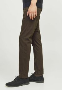 Pantaloni in cotone marrone con una vestibilità slim, dotati di due tasche frontali e cuciture visibili. Abbinati a scarpe in camoscio nere.