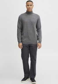 Grijze coltrui met een textuur, gecombineerd met donkere, loszittende broeken en zwarte sneakers.