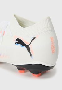 Weißer Fußballschuh mit einem strukturierten Strick-Obermaterial, schwarzen und korallenfarbenen Akzenten sowie einer kontrastierenden schwarzen Sohle mit orangenen Noppen. Puma-Logo angezeigt.
