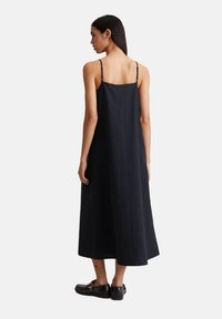 Schwarzes ärmelloses Kleid mit dünnen Trägern, lockerer Passform und Midi-Länge. Hergestellt aus strukturiertem Stoff mit einem schlichten, ungeschmückten Design.