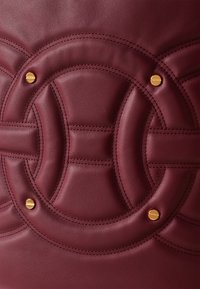 Burgundy leather bag featuring quilted circular patterns, gold hardware accents, and detailed stitching. Smooth texture with distinct shapes.