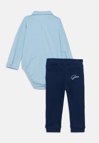 Ανοιχτό μπλε μακρυμάνικο κορμάκι με γιακά και κουμπωτά μανίκια, σε συνδυασμό με σκούρο μπλε παντελόνι φόρμας με δύο πίσω τσέπες και λογότυπο.