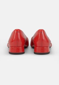 Zapatos de charol rojo con punta redonda y un pequeño tacón cuadrado. Textura suave y detalles de costura mínimos en la parte trasera.