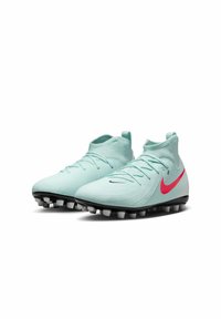 Une paire de chaussures de soccer bleu clair avec un logo Nike rose, présentant un design épuré et des crampons en caoutchouc moulés pour une meilleure adhérence sur le terrain.