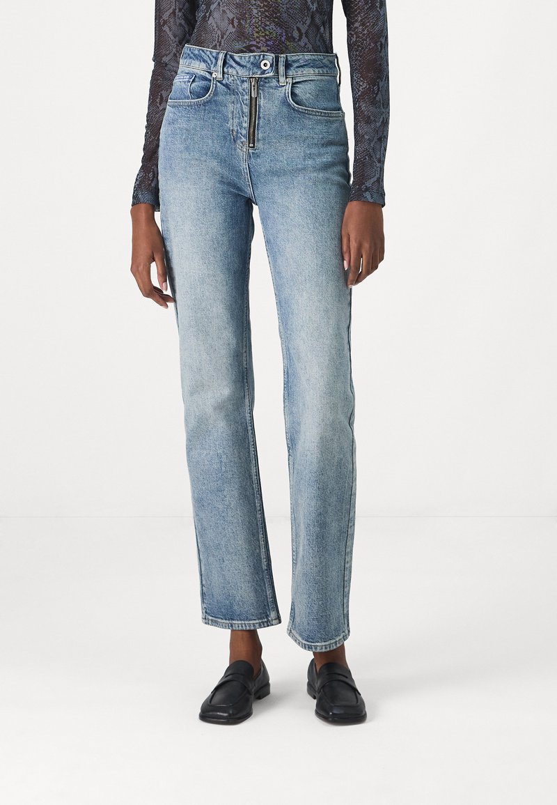 Lichtblauwe denim jeans met een recht design, voorzien van een rits en een riemlussen, en subtiele vervaging. G gedragen met zwarte instappers.