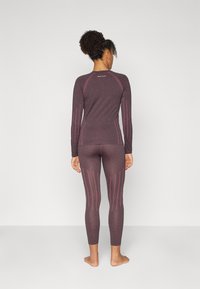 Tight sittande träningsset i mörklila med kontrasterande rosa vertikala ränder, långärmad topp och leggings, slät yta, ingen synlig hårdvara.