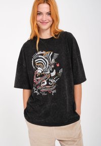 Camiseta negra de gran tamaño con un acabado texturizado, que presenta un diseño gráfico colorido de animales y formas en el frente.
