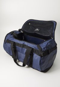 Navy blue duffel bag with black accents, made of durable fabric. Features two sturdy handles, a zippered main compartment, and mesh pockets inside.