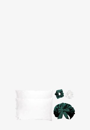 Deux taies d'oreiller en satin blanc, un bonnet en satin vert foncé avec un nœud noué, et deux chouchous en satin, un vert foncé et un blanc, sur un fond blanc.