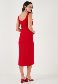 Abito midi rosso aderente con scollatura a barca, caratterizzato da una texture liscia. Abbinato a sandali rossi con tacco a blocco. Design semplice senza decorazioni.