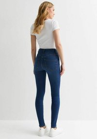 Vaqueros de mezclilla azul de cintura alta con un diseño ajustado, que presentan bolsillos traseros y detalles de costura sutiles, combinados con una camiseta de algodón blanca de canalé.