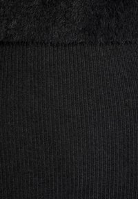 Zwarte leggings met een gladde, geribbelde textuur en een zachte, pluizige bovenkant. Over het algemeen één kleur zonder verdere patronen of accenten.