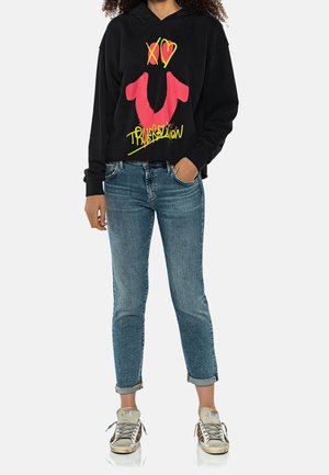 Černá mikina s kapucí s růžovo-žlutým grafickým motivem, doplněná světle modrými vyhrnutými džínami a šedými teniskami. Pohodlný střih, bavlněný materiál.