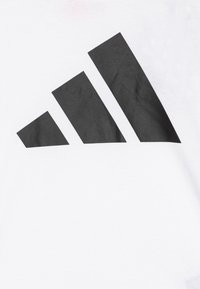 Camiseta blanca con un gran logo negro de tres rayas en el frente. La tela es suave con un ligero brillo.