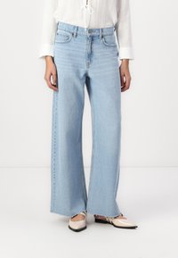 Blugi largi, de culoare albastru deschis, fabricați din denim, cu talie înaltă și o estompare subtilă. Dedicația este brută, având o textură ușor deteriorată.