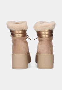 Botas de tacón alto beige con un collar de piel sintética y acentos dorados, presentando una textura suave y un diseño de cordones. Suela de plataforma gruesa.