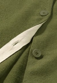 Oliivinvihreä kangas, jossa on ribbitekstuuri, ja sisäreunassa on kaksi vihreää nappia ja valkoinen herringbone-nauha.