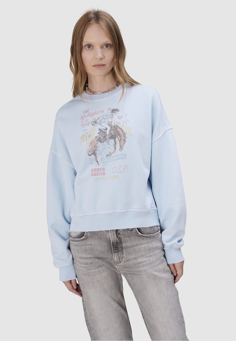 Jasnoniebieska bluza z grafiką przedstawiającą scenę rodeo. Ma luźny krój, ściągacze na rękawach oraz krótki dół.