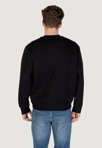 Sudadera negra con cuello redondo y puños acanalados, combinada con jeans de color azul claro que cuentan con costuras en los bolsillos traseros. Textura de tela suave.