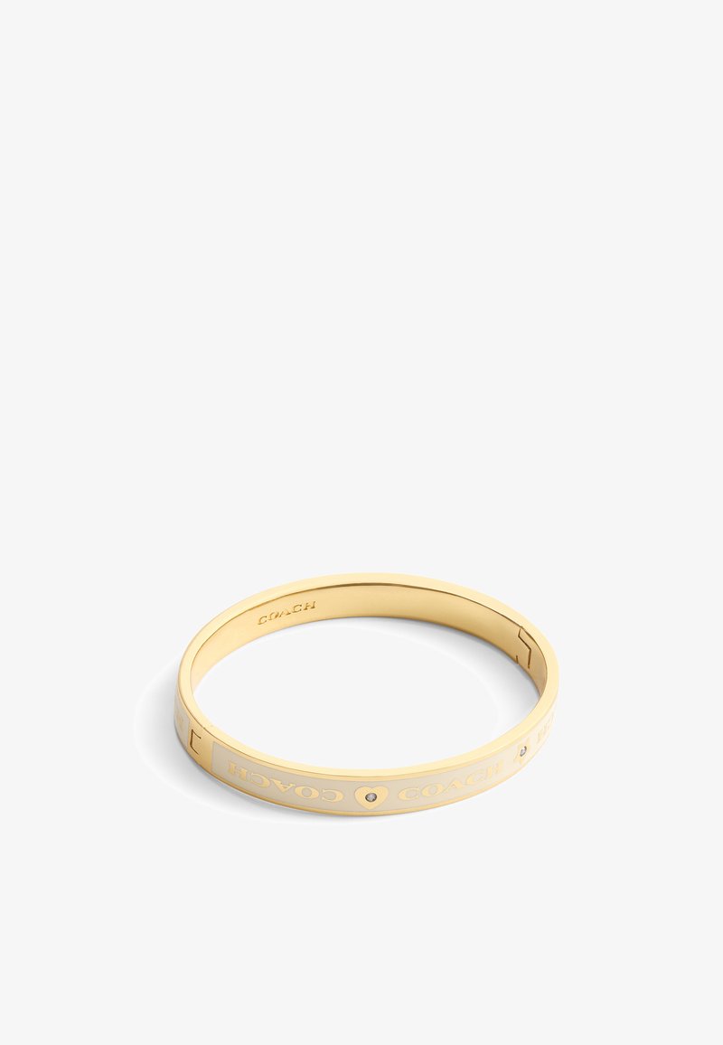 Bracelet jonc doré avec inscription gravée « COACH » et design en forme de cœur, finition lisse et une petite pierre d'accent.