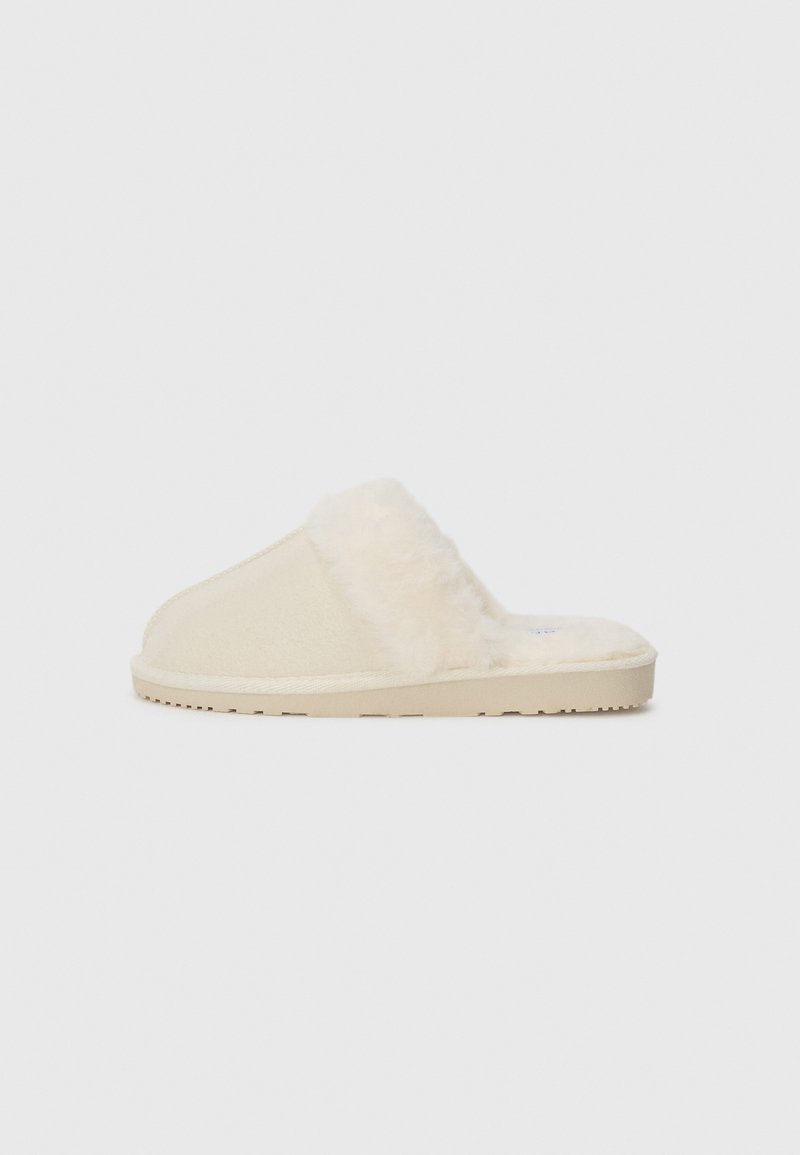 Beige fluffiga tofflor med mjuk yta, med en plyschöverdel och en texturerad gummisula för bra grepp.