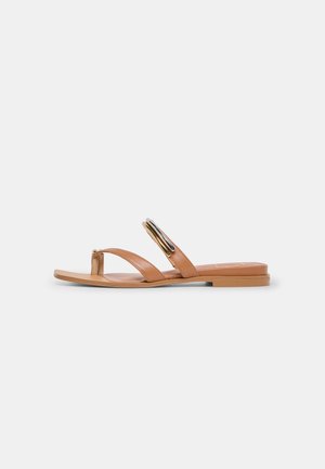 Platte sandalen in beige met teenlus en twee bandjes, waarvan één met een goud-zwart ovale gesp.
