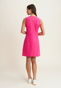 Vestido sin mangas rosa con detalle de abertura en la parte posterior, ajuste estructurado y textura suave. Combinado con zapatillas blancas de plataforma.