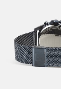 Svart mesh klokkerem med en strømlinjeformet metallspenne. Har et strukturert mønster som sikrer en solid passform og moderne design. Minimalistisk utseende.