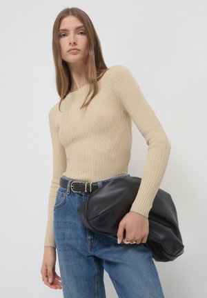 Beige Rippenoberteil mit langen Ärmeln und figurbetonendem Design, kombiniert mit hochtaillierten blauen Jeans. Hält eine große schwarze Lederhandtasche.