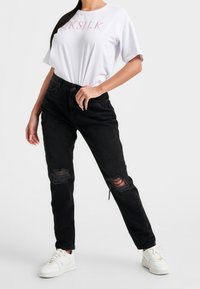 Bílý krátký rukáv tričko s textem "SILK", spárované s černými roztrhanými džíny a bílými teniskami. Ležérní střih s opotřebenými detaily na kalhotách.