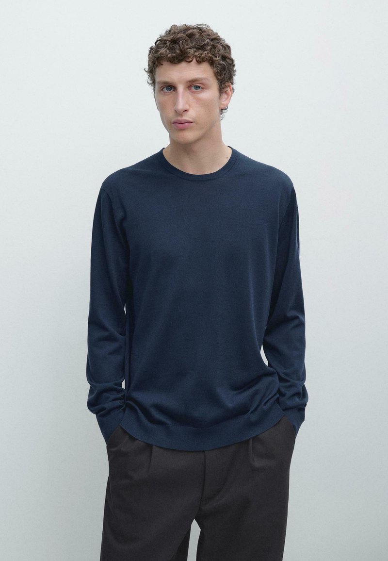 Maglia a maniche lunghe blu navy in tessuto morbido, scollo tondo, vestibilità comoda, con cuciture sottili, abbinata a pantaloni scuri. Tessuto liscio, design minimale.