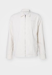 Balta zip-up striukė, pagaminta iš minkštos medžiagos. Sukurta su smailiu apykakle, ilgomis rankovėmis ir subtiliu logotipu ant krūtinės.
