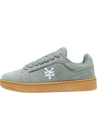 Grå semsket sneaker med en hvit logo, rund tå og gummisåle. Har grå snører og en polstret kant for komfort.