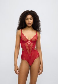 Κόκκινο διαφανές κορμάκι με δαντελένιες λεπτομέρειες, ντεκολτέ με κυματιστό τελείωμα, διασταυρούμενη λεπτομέρεια μπροστά και πλαϊνές ανοίγματα. Μαλακή, ευαίσθητη υφή.