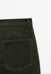 Pantalon en velours côtelé vert foncé montrant la poche arrière, la ceinture avec passants et les surpiqûres visibles sur fond blanc.
