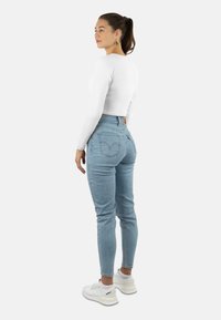 Hellblau hohe Jeans mit Slim Fit, Denim-Material und Gesäßtaschen. Kombiniert mit einem weißen Langarm-Crop-Top und weißen Turnschuhen.