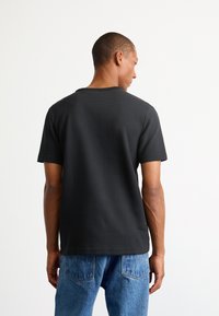 Must mustärga lühikese varrukaga T-särk, millel on tekstuuriga kangas, ümmargune kaelus ja mugav lõige, kokku sobitatud heledate siniste teksadega.