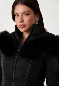 Black puffer jacket with a shiny finish, featuring a large, soft black faux fur collar and diagonal quilted pattern on the body.