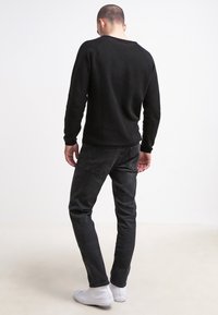 Pull noir à manches longues et jean foncé coupe slim. Baskets blanches, texture lisse et design basique sans motifs ni accents visibles.