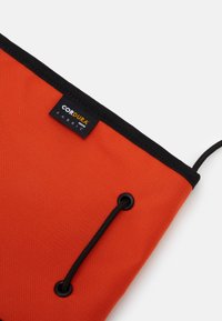 Custodia in Cordura arancione con accenti neri; presenta un'etichetta con il marchio "Cordura" e una chiusura con coulisse vicino a un occhiello rinforzato.
