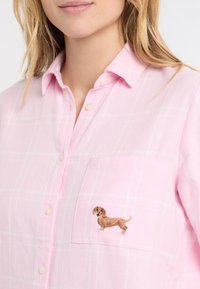 Różowa koszula w kratę na guziki z kieszenią na piersi, ozdobioną haftowanym brązowym jamnikiem. Miękki materiał o lekkiej fakturze i zaokrąglonym kołnierzyku.