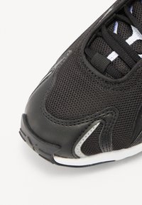 Baskets de sport noires avec une tige en maille, des accents en simili cuir, un bout arrondi et une semelle texturée avec des détails blancs.