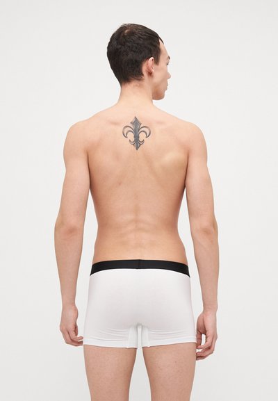 Weiße Boxer-Briefs aus weichem Material mit einem schwarzen elastischen Bund. Das Modell hat kurze Haare und ein Tattoo auf dem Rücken.