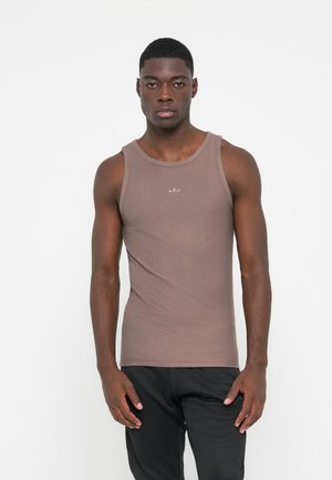 Brun ribbet tanktop med rund halsudskæring og diskret branding på brystet, parret med sorte bukser. Tætsiddende design der fremhæver armene.