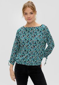Bluse mit floralem Muster in Türkis, Schwarz und Grün. Merkmale sind ein Bootsausschnitt und geraffte Bündchen mit Bändern. Leichtes, fließendes Material.