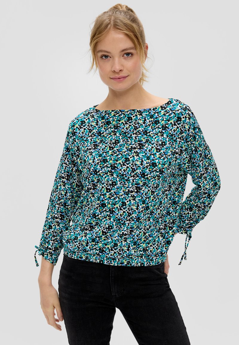 Bluse mit floralem Muster in Türkis, Schwarz und Grün. Merkmale sind ein Bootsausschnitt und geraffte Bündchen mit Bändern. Leichtes, fließendes Material.