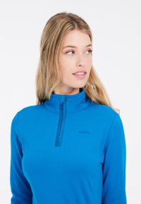 Långärmad, dragkedjestopp i ljusblått. Tillverkad av slätt, elastiskt material med hög krage och broderad "protest"-logotyp på bröstet.