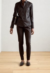 Svart skjorta med knappar och en strukturerad krage, i kombination med slim-fit svarta byxor. Vadderade axeldetaljer och svarta loafers med guldfinish.